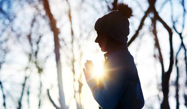 Silhouette of a meditating woman in the forest with a sun light in her hands
